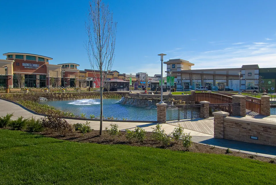 Retail pond edge with lawn, stone wall, planting beds, storefronts, and bridge structure